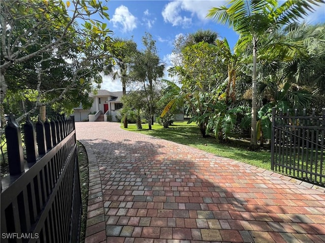 view of property's community with decorative driveway, fence, and a lawn