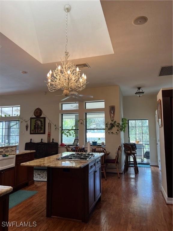 kitchen featuring light stone counters, decorative light fixtures, a center island, dark hardwood / wood-style floors, and stainless steel gas stovetop