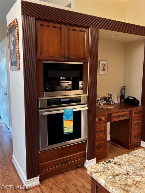 kitchen with light stone countertops, light hardwood / wood-style flooring, and oven