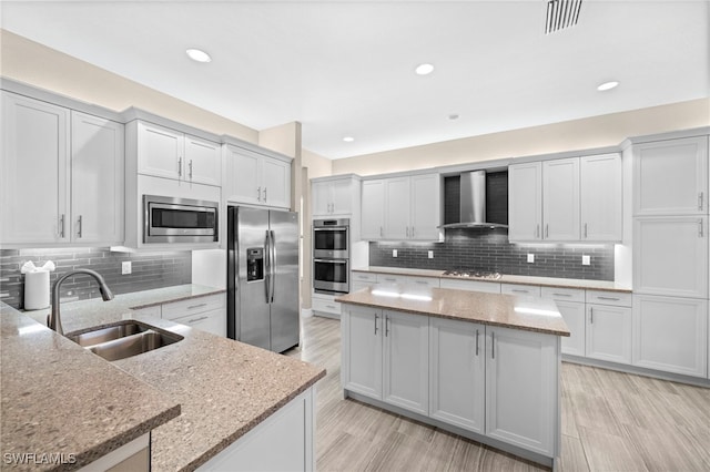 kitchen featuring sink, a center island, light stone counters, stainless steel appliances, and wall chimney range hood