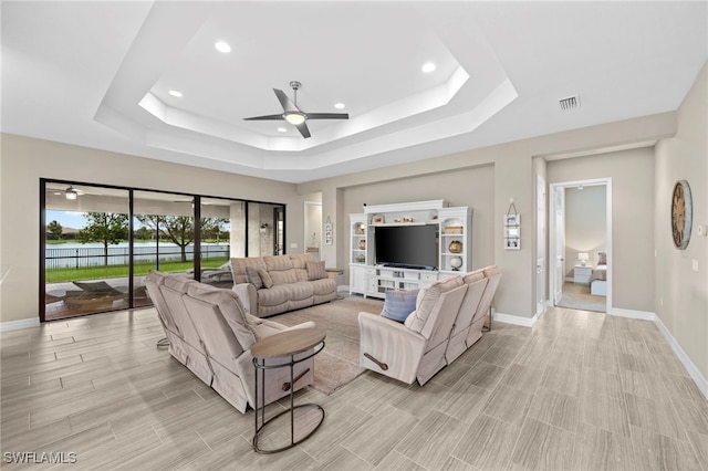 living room with a raised ceiling and ceiling fan