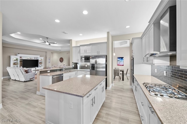 kitchen featuring sink, a center island, light stone counters, stainless steel appliances, and wall chimney range hood