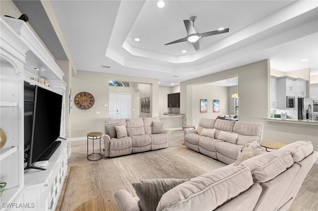 living room with ceiling fan, a raised ceiling, and light hardwood / wood-style floors