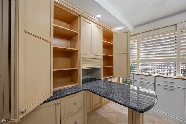 kitchen featuring built in desk, cream cabinetry, light tile patterned floors, and dark stone counters