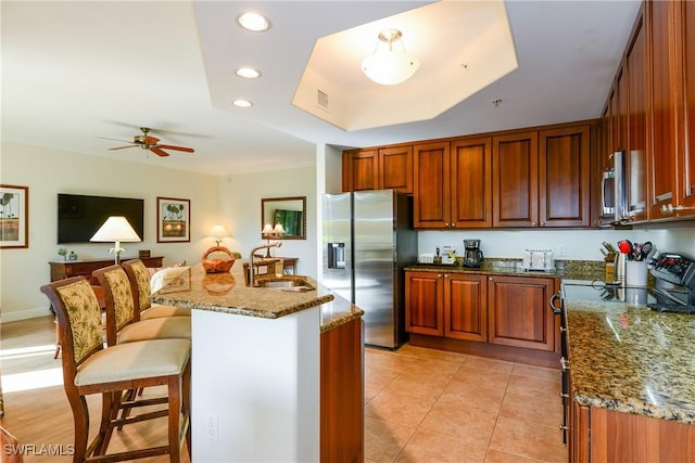 kitchen featuring a kitchen bar, stainless steel appliances, a tray ceiling, dark stone counters, and sink