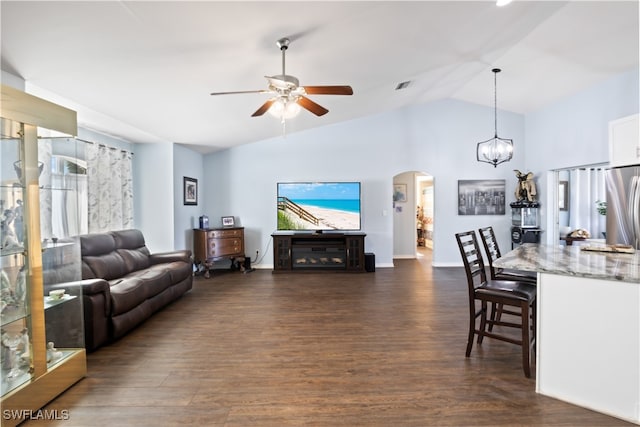 living room featuring dark wood-type flooring, ceiling fan with notable chandelier, and vaulted ceiling