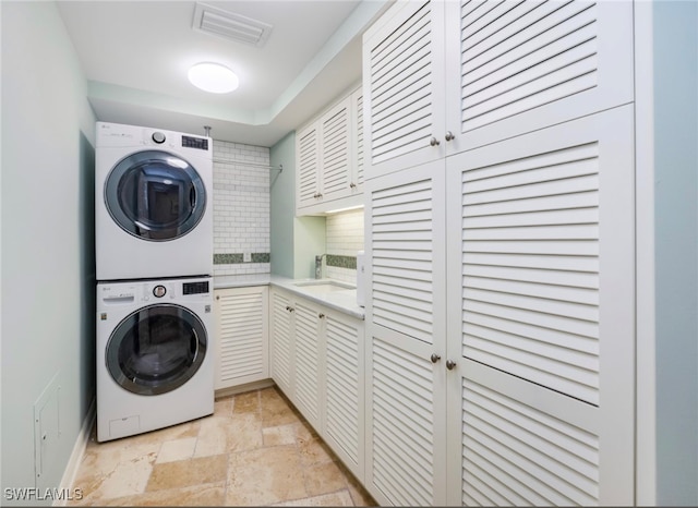 clothes washing area featuring stacked washing maching and dryer and cabinets