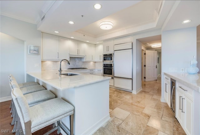 kitchen featuring kitchen peninsula, white cabinets, backsplash, a breakfast bar area, and sink