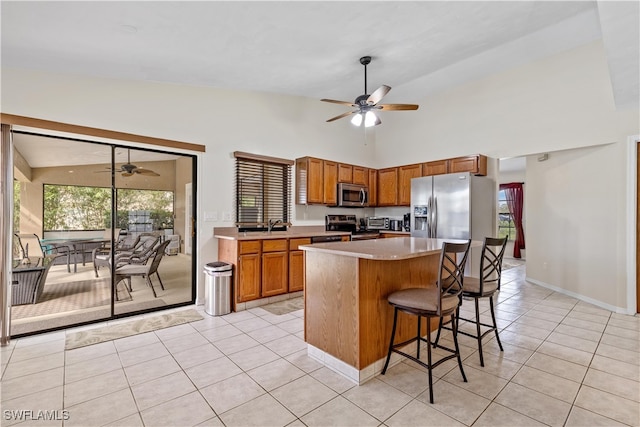 kitchen featuring ceiling fan, appliances with stainless steel finishes, a breakfast bar, light tile patterned flooring, and a center island