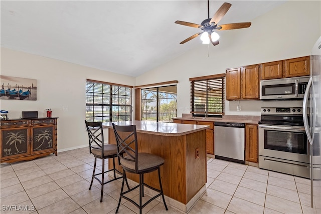 kitchen featuring appliances with stainless steel finishes, a center island, light tile patterned floors, and vaulted ceiling