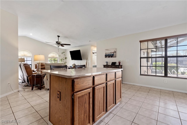 kitchen with ceiling fan, lofted ceiling, a center island, and light tile patterned floors