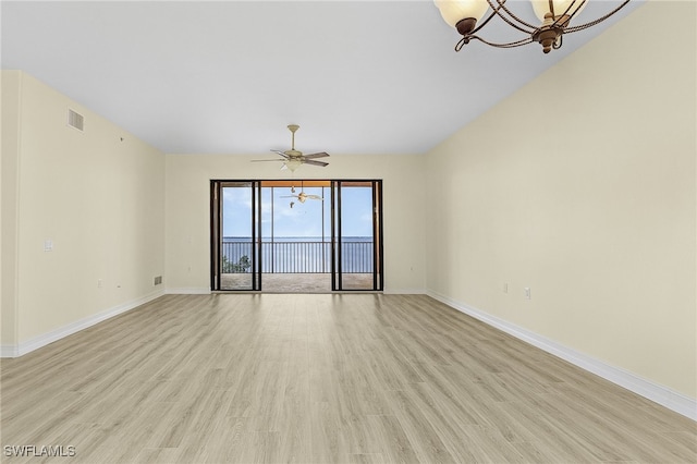 empty room with ceiling fan with notable chandelier and light wood-type flooring