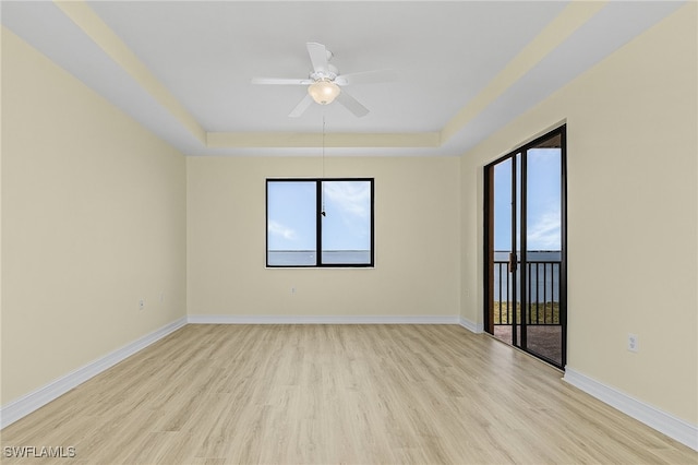 unfurnished room with ceiling fan, a tray ceiling, and light hardwood / wood-style flooring