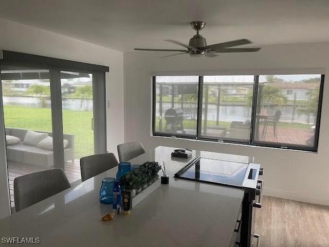 dining room featuring a ceiling fan, wood finished floors, a water view, and baseboards