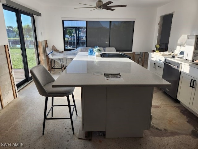 kitchen with a ceiling fan, a kitchen island, white cabinets, dishwasher, and a kitchen breakfast bar