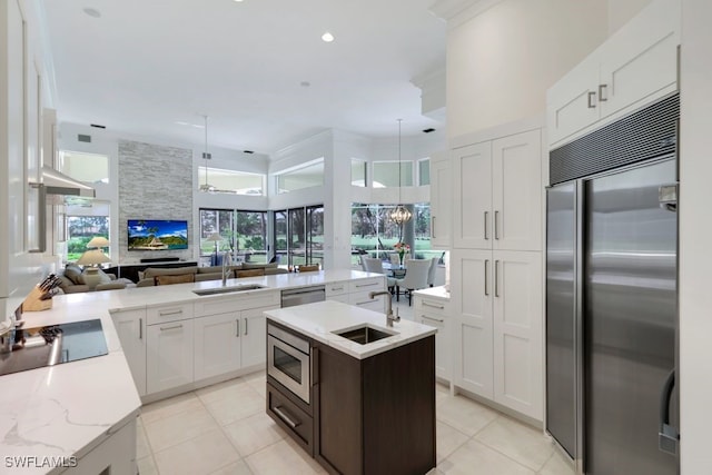 kitchen featuring open floor plan, a kitchen island with sink, a sink, built in appliances, and a peninsula