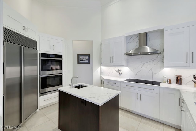 kitchen with a sink, appliances with stainless steel finishes, backsplash, wall chimney exhaust hood, and a center island with sink