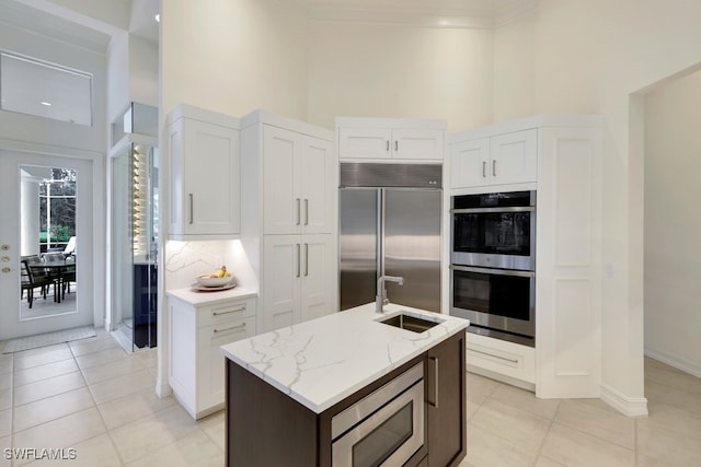 kitchen with white cabinets, a sink, a towering ceiling, and built in appliances