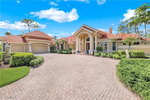 mediterranean / spanish house with decorative driveway, a tile roof, a chimney, stucco siding, and a garage