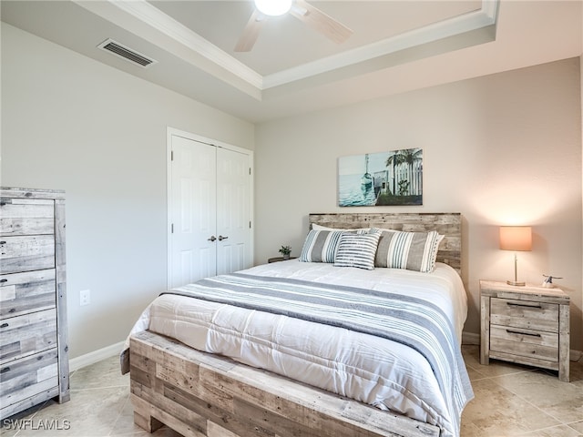 bedroom featuring ornamental molding, a tray ceiling, ceiling fan, light tile patterned floors, and a closet