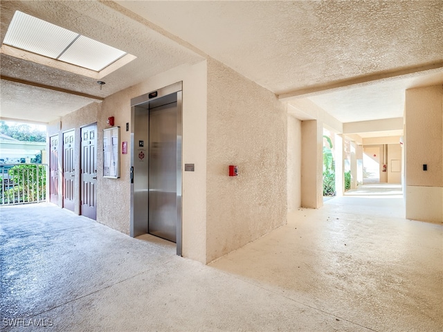 hall with elevator, a wealth of natural light, and a textured ceiling