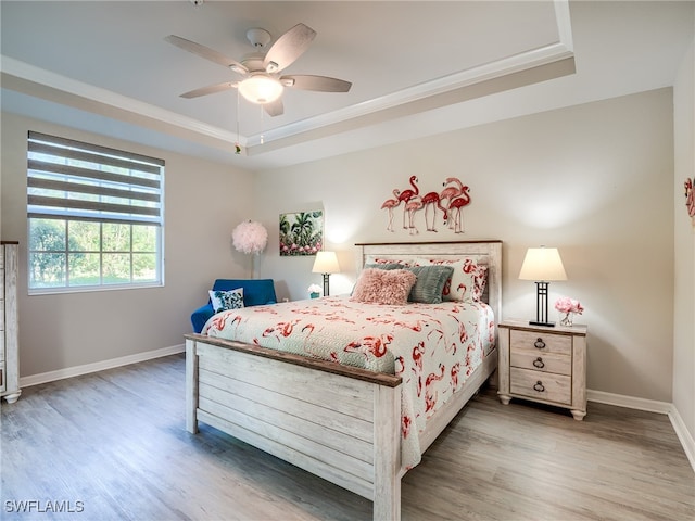 bedroom with hardwood / wood-style floors, a tray ceiling, ceiling fan, and ornamental molding