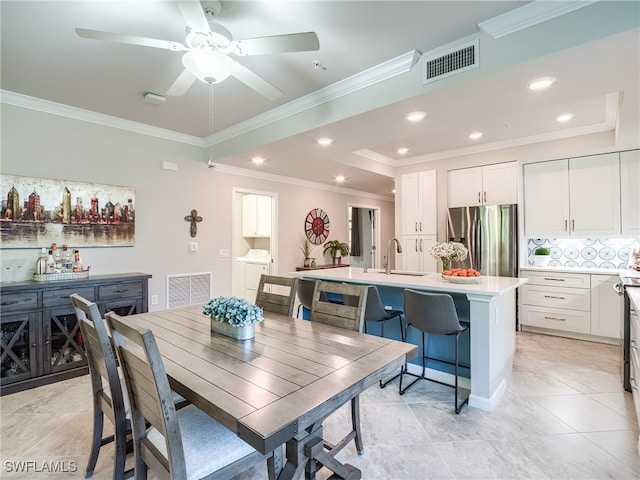 tiled dining space with a raised ceiling, crown molding, sink, ceiling fan, and independent washer and dryer