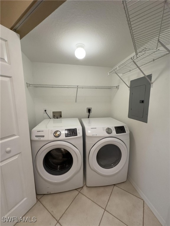 washroom featuring independent washer and dryer, a textured ceiling, electric panel, and light tile patterned flooring