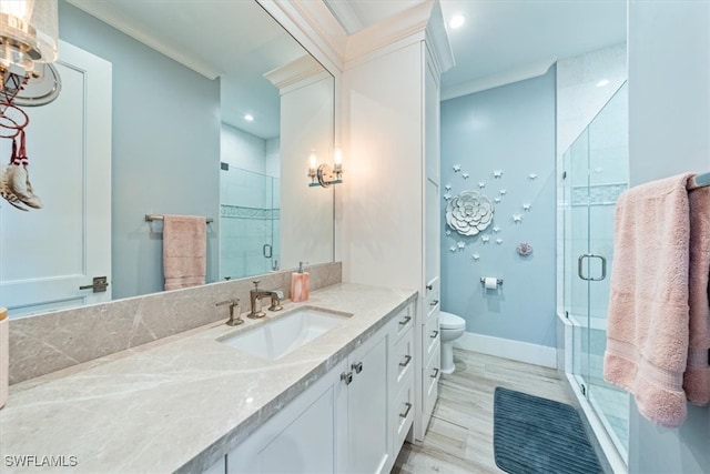 bathroom featuring wood-type flooring, toilet, a shower with door, vanity, and crown molding