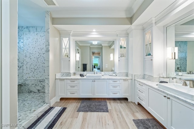 bathroom with vanity, wood-type flooring, crown molding, and a tile shower