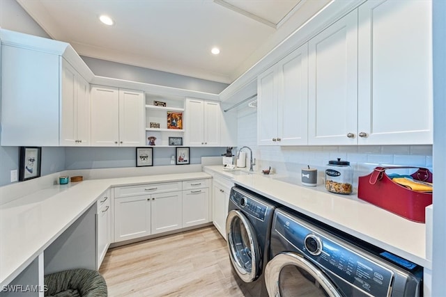 clothes washing area with light wood-type flooring, cabinets, sink, and washer and dryer