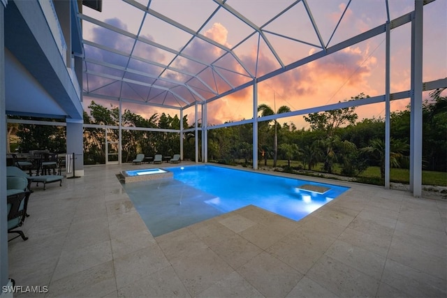 pool at dusk featuring glass enclosure, a patio area, and an in ground hot tub