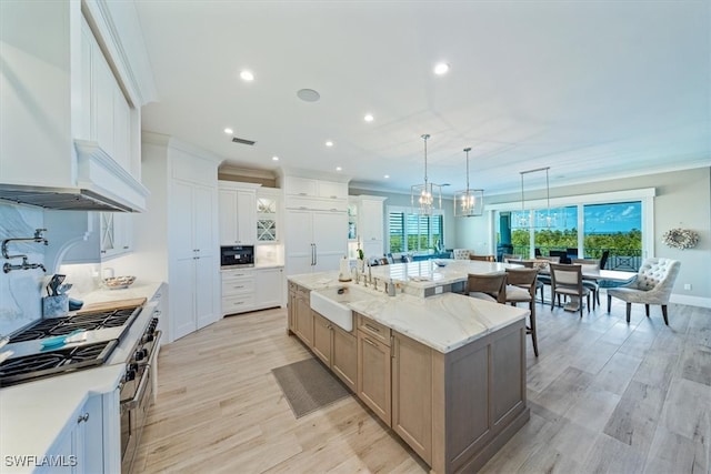 kitchen featuring a wealth of natural light, sink, a large island with sink, and white cabinets