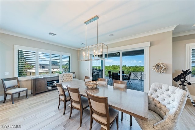 dining space with light wood-type flooring, an inviting chandelier, and ornamental molding