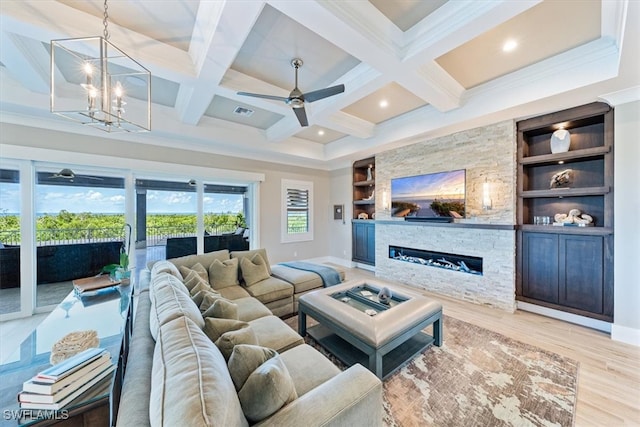 living room featuring built in shelves, beam ceiling, a stone fireplace, coffered ceiling, and light wood-type flooring