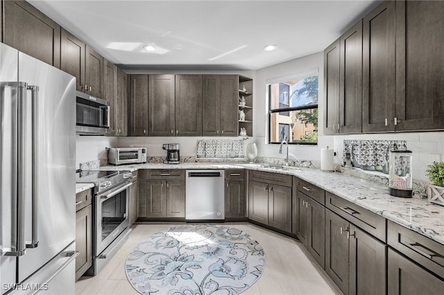 kitchen with backsplash, sink, light stone countertops, dark brown cabinetry, and appliances with stainless steel finishes