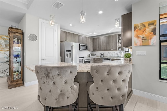 kitchen featuring a kitchen breakfast bar, kitchen peninsula, decorative light fixtures, light wood-type flooring, and appliances with stainless steel finishes