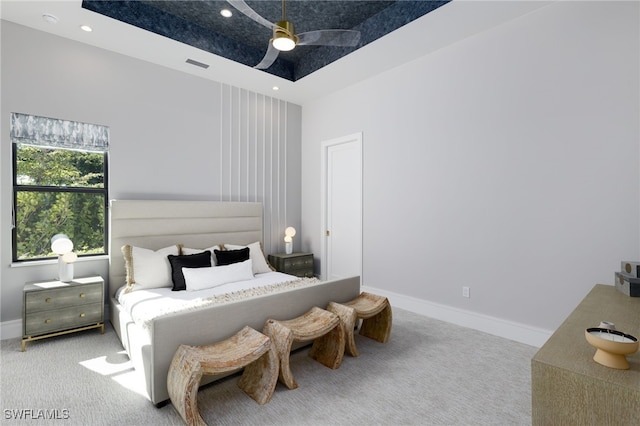 carpeted bedroom with ceiling fan and a raised ceiling