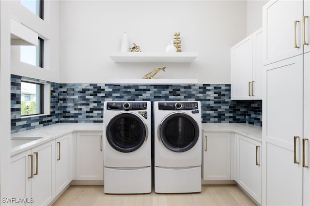 clothes washing area featuring washer and dryer, light wood-type flooring, and cabinets