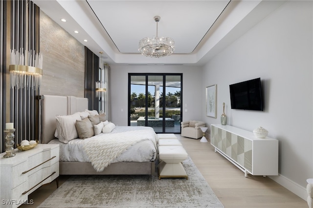 bedroom featuring light wood-type flooring, access to outside, a tray ceiling, and a chandelier