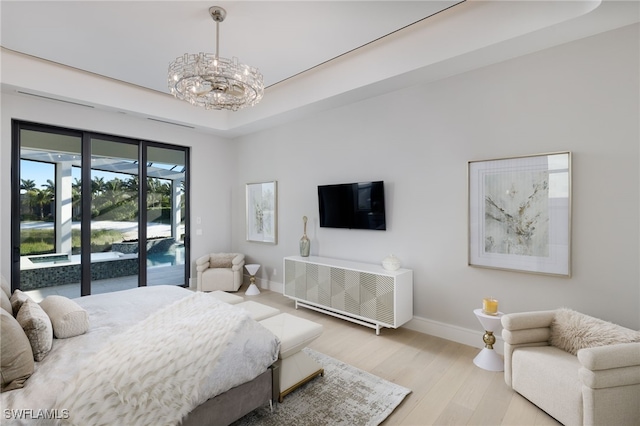 bedroom featuring a tray ceiling, light hardwood / wood-style flooring, a chandelier, and access to exterior