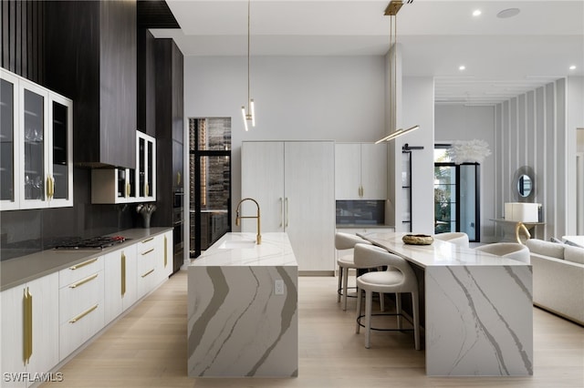 kitchen featuring a large island with sink, decorative light fixtures, and white cabinets