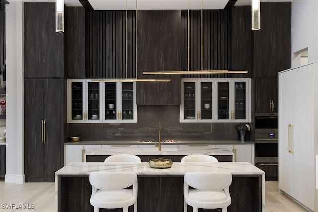 kitchen featuring backsplash, a center island, a kitchen breakfast bar, hanging light fixtures, and light stone counters