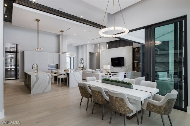 dining room with light hardwood / wood-style floors, an inviting chandelier, sink, and a high ceiling