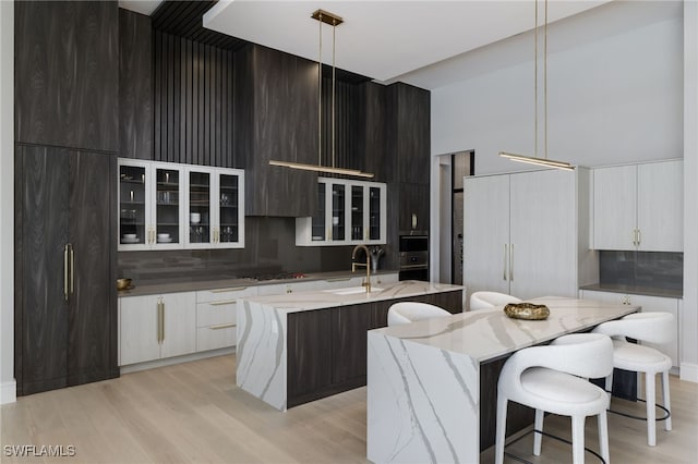 kitchen with a center island with sink, sink, hanging light fixtures, and light wood-type flooring