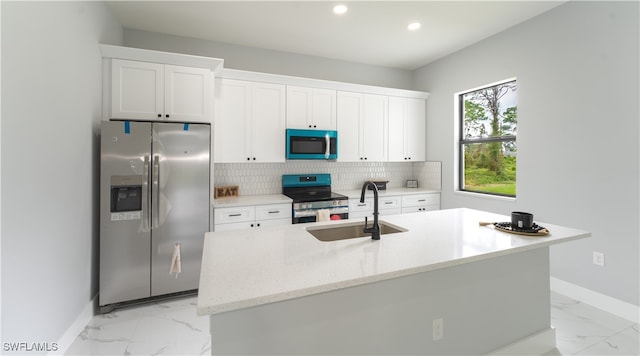 kitchen with appliances with stainless steel finishes, white cabinetry, sink, and an island with sink