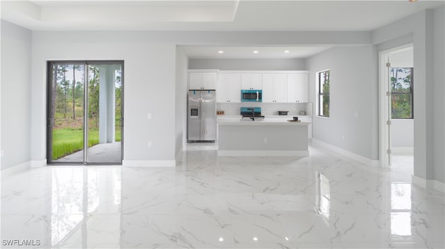 kitchen with stainless steel appliances, a kitchen island with sink, decorative backsplash, and white cabinets