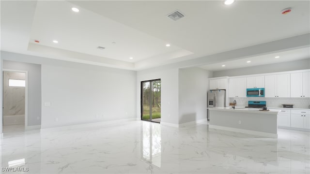 kitchen with white cabinetry, stainless steel appliances, a tray ceiling, and an island with sink