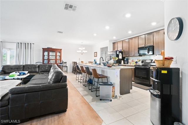 kitchen featuring a center island with sink, backsplash, a breakfast bar, black appliances, and pendant lighting