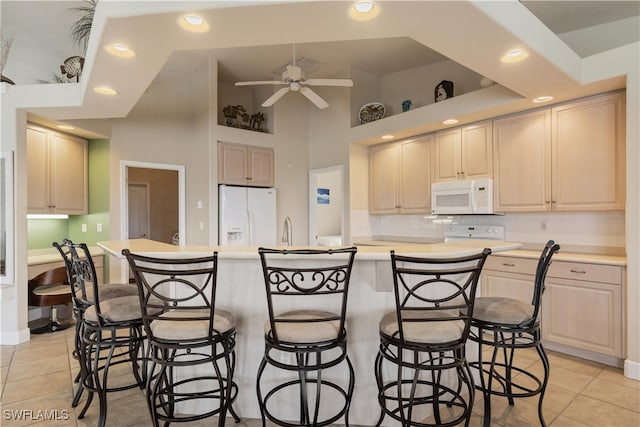 kitchen with light tile patterned flooring, a kitchen island with sink, white appliances, and ceiling fan